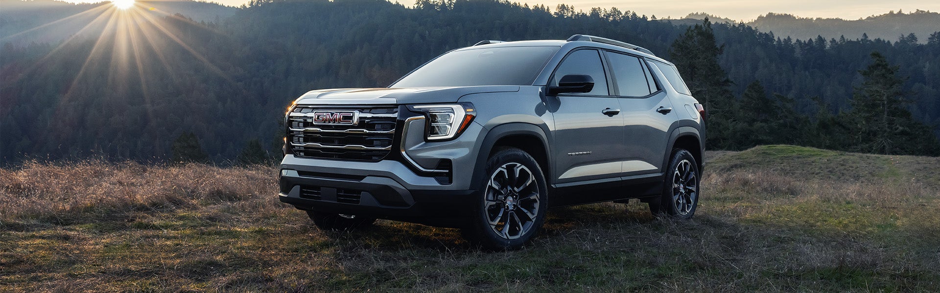 GMC Terrain SUV parked on a grassy hillside with a forest landscape in the background